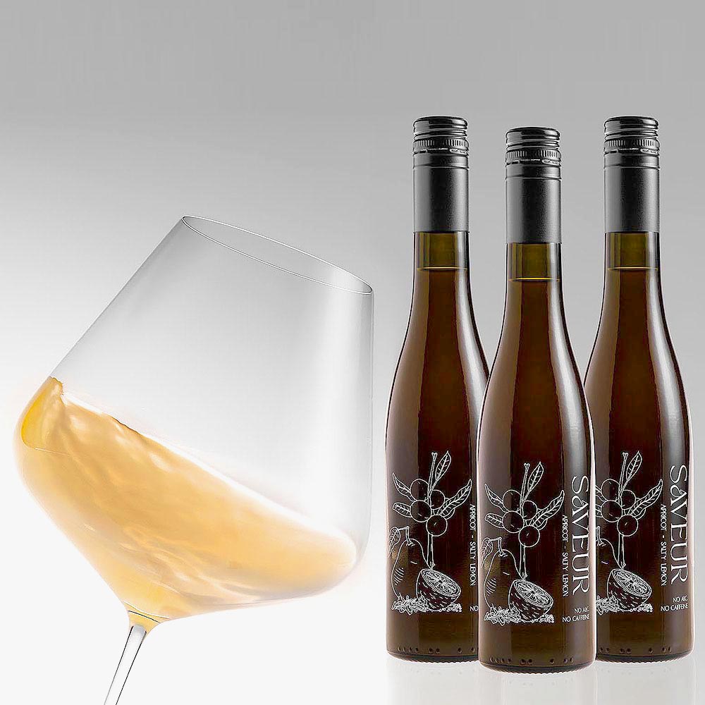 ein halbvolles weinglass mit weisswein und drei geschlossenen weinflaschen auf grauem hintergrund